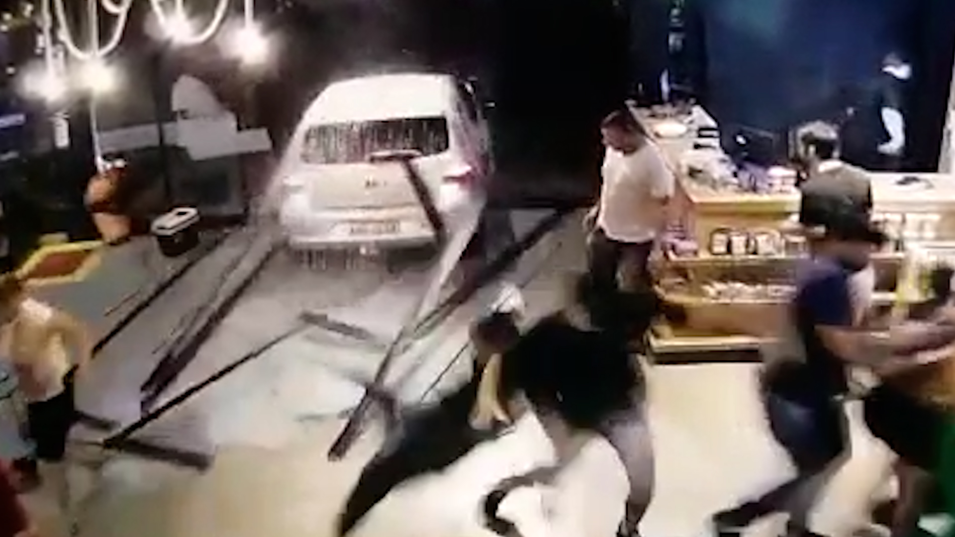  Imagem retirada de vídeo gravado por câmera de segurança do local, no exato momento em que o veículo destrói as portas de vidro do local, fazendo com que várias pessoas saiam correndo 