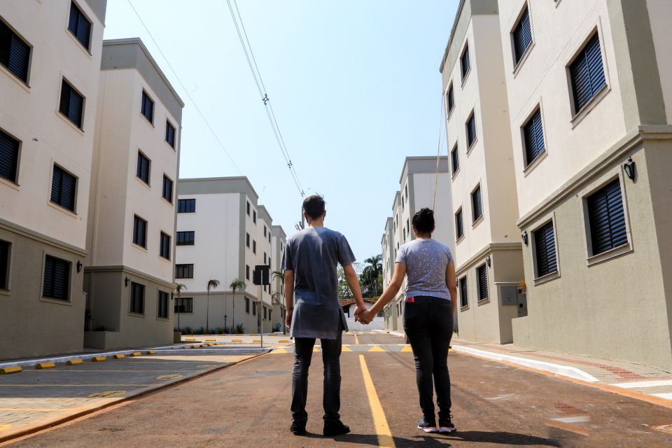  Casal de costas e mãos dadas observando um compilado de prédios residenciais 