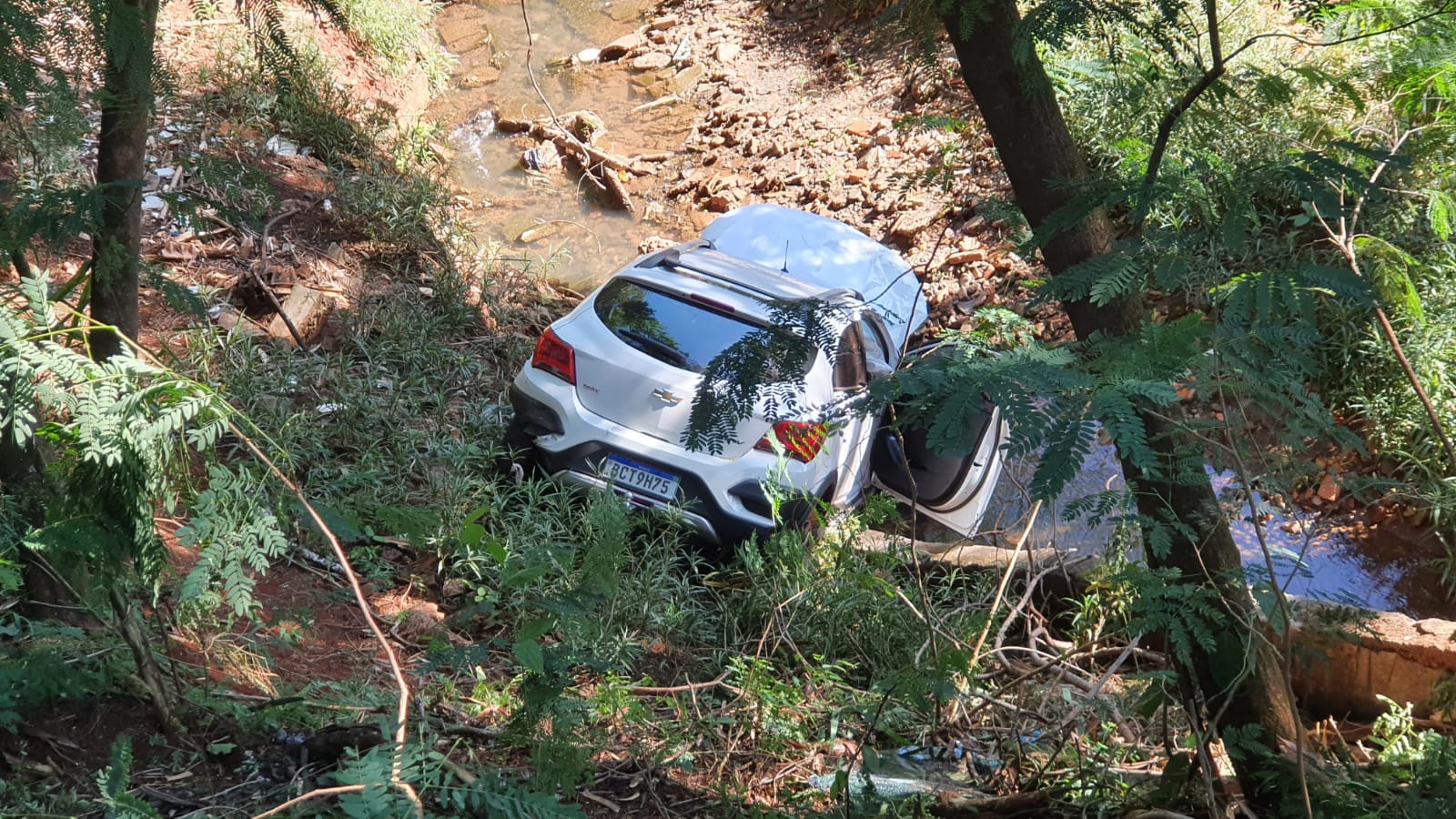  Veículo branco no fundo de um vale, com um pequeno riacho à frente 