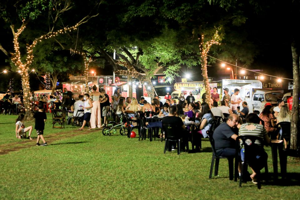  food trucks na praça da Catedral em Maringá durante a noite com clientes sentados em mesas 