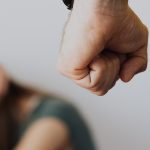 Punho masculino fechado e mulher com as mãos na frente do rosto ao fundo