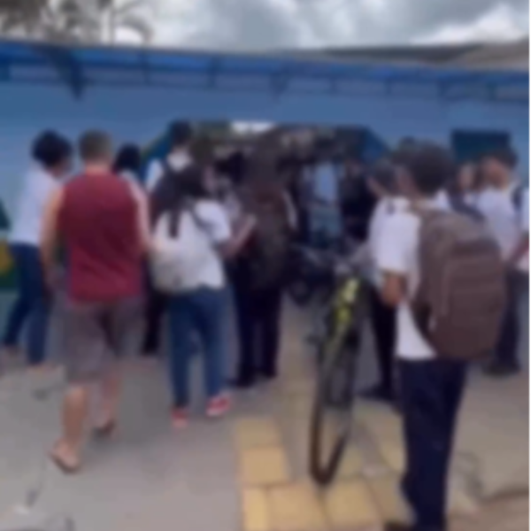 pessoas reunidas assistindo a uma briga em frente a uma escola estadual