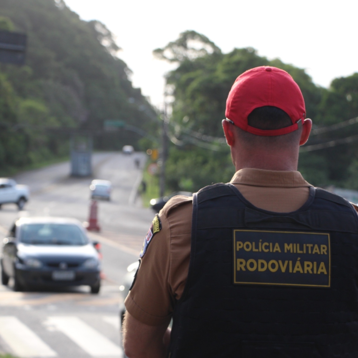  policial de costas monitorando trânsito de veículos em rodovia 